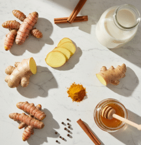 Ingredients for turmeric latte scattered on a marble counter: fresh turmeric root, almond milk, ginger slices, and honey jar, top-down shot in 4K with natural sunlight filtering through for a fresh, healthy feel.